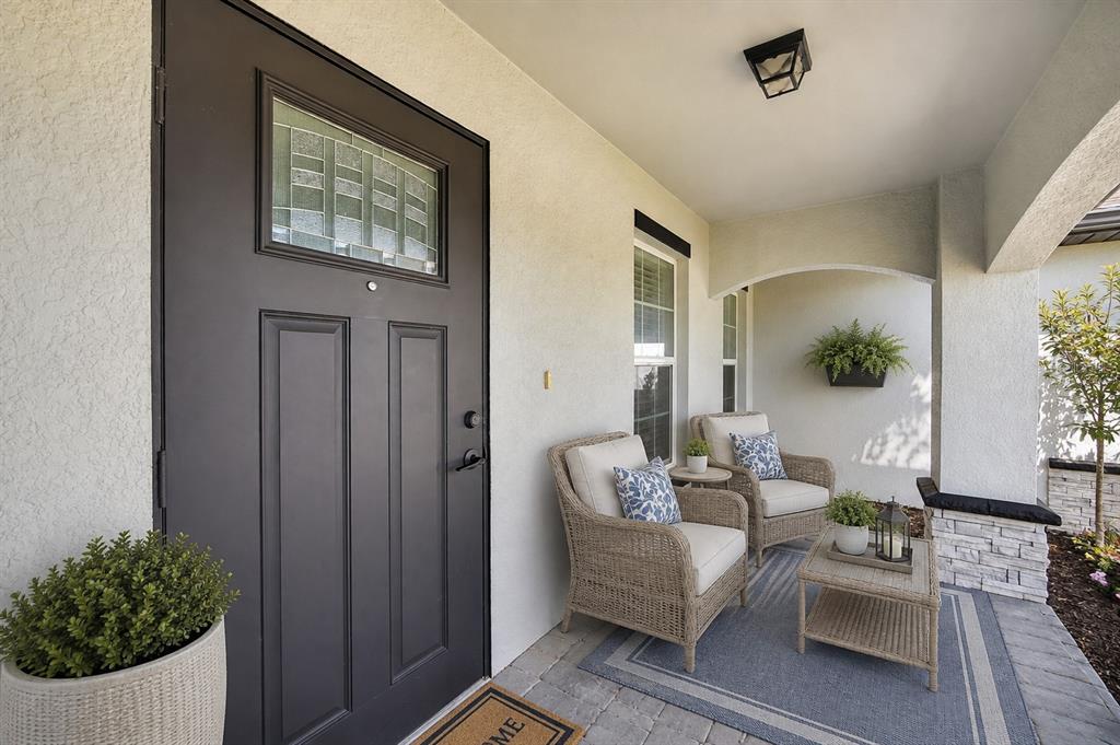 A covered front porch features a dark door, two wicker chairs, and a small table — 4238 NW 34TH LANE, CAPE CORAL, FL