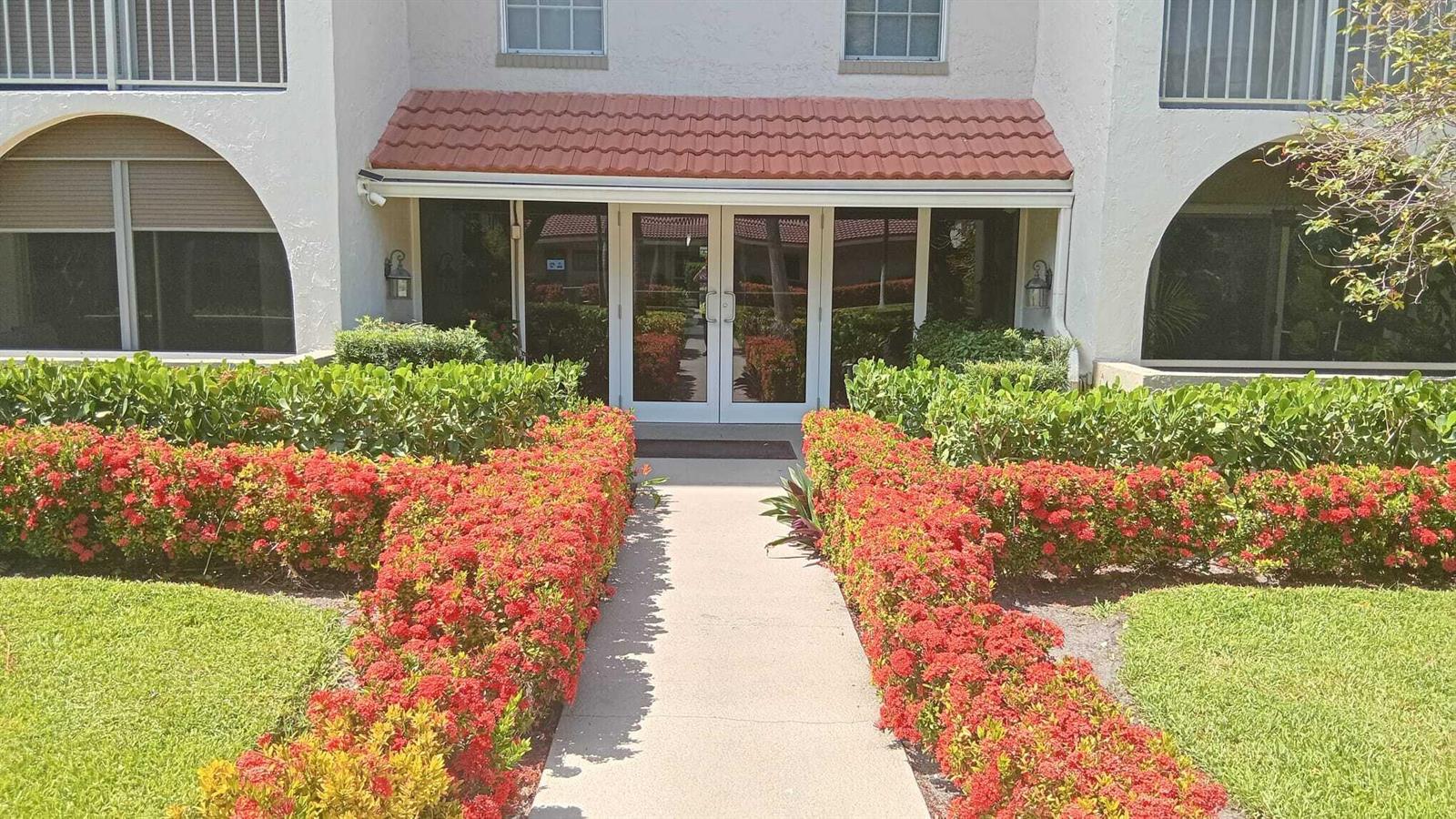 A concrete walkway leads to the glass double-door entrance of a building with red-tiled roofing — 250 NE 20th Street # 3080, Boca Raton FL 33431, BOCA RATON, FL
