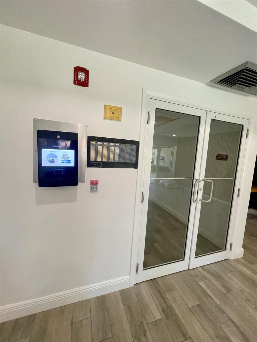 A white wall features a digital intercom system, a fire alarm, and double glass doors — 250 NE 20th Street # 3080, Boca Raton FL 33431, BOCA RATON, FL