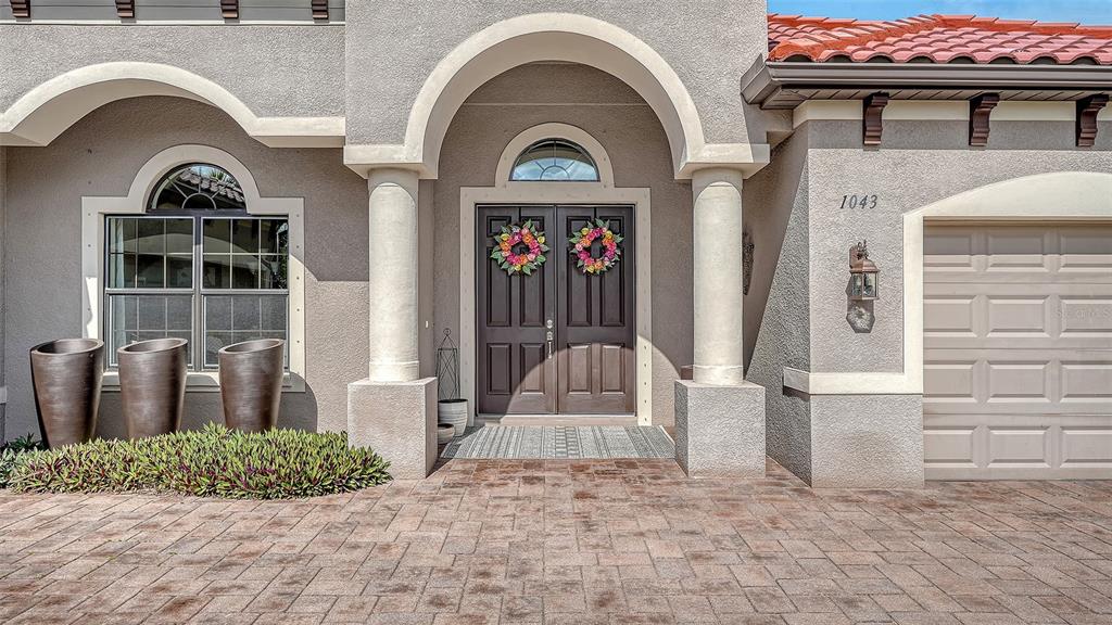 A beige stucco house exterior features a double front door, arched entryway, and paver driveway — 1043 145TH STREET CIRCLE NE, BRADENTON, FL