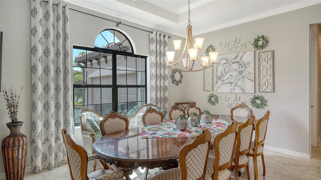 A dining room features a wooden table, patterned chairs, a chandelier, and a large window — 1043 145TH STREET CIRCLE NE, BRADENTON, FL