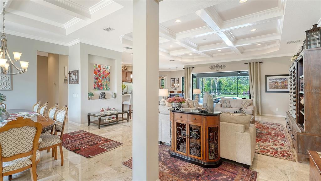 An open-concept living and dining area features coffered ceilings, tile flooring, and a rear patio — 1043 145TH STREET CIRCLE NE, BRADENTON, FL