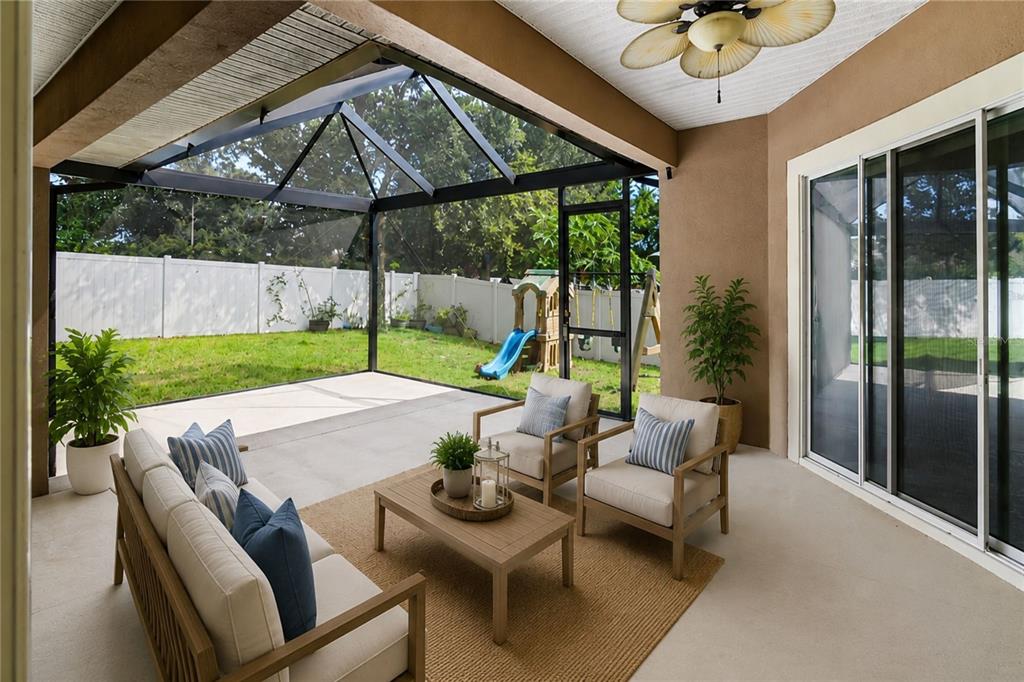 A covered patio features a screened-in enclosure, outdoor furniture, and a view of the backyard — 410 SAUVIGNON WAY, GROVELAND, FL