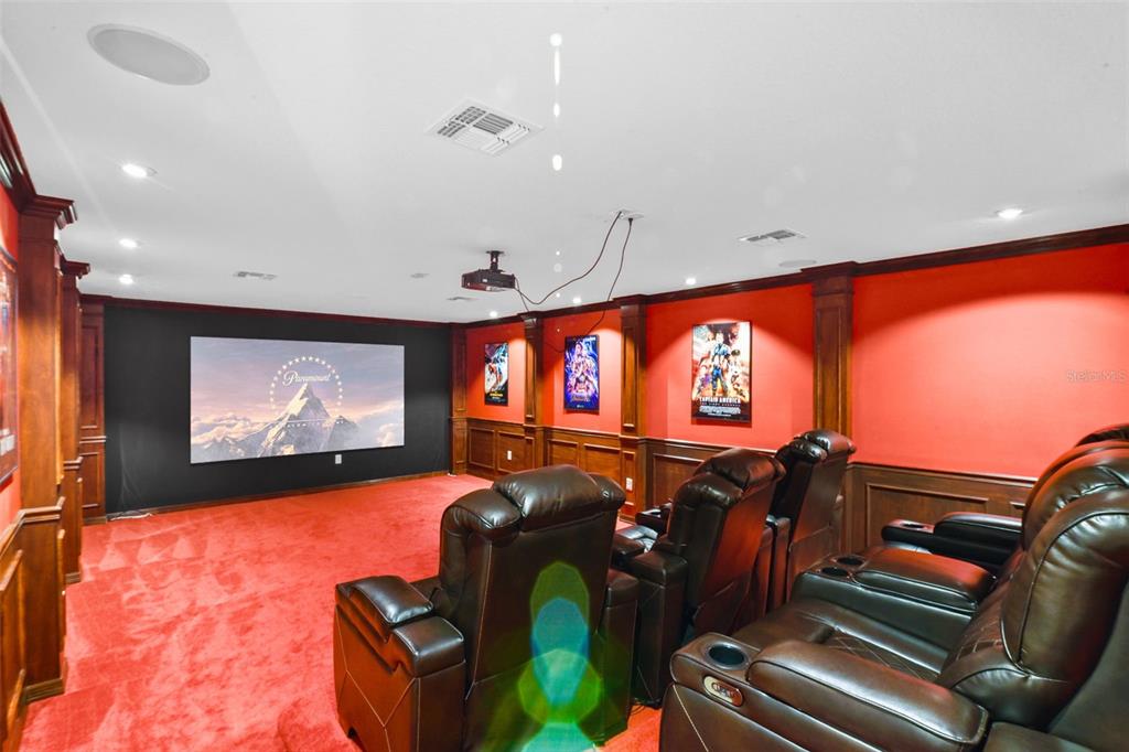 A home theater features red walls, dark wood trim, tiered leather seating, and a projector screen — 410 SAUVIGNON WAY, GROVELAND, FL