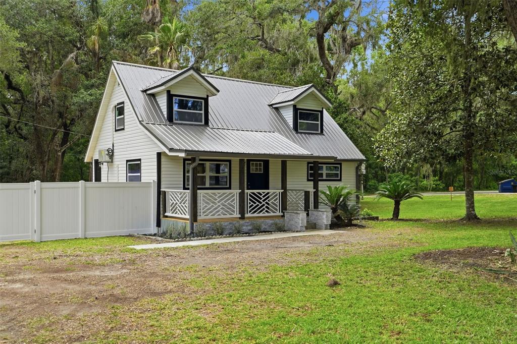 A white two-story cottage with a metal roof and a front porch sits on grass — 14335 SNOW MEMORIAL HIGHWAY, BROOKSVILLE, FL