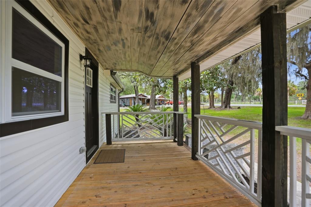 A covered wooden porch features decorative white railings and a rustic, stained wood ceiling — 14335 SNOW MEMORIAL HIGHWAY, BROOKSVILLE, FL