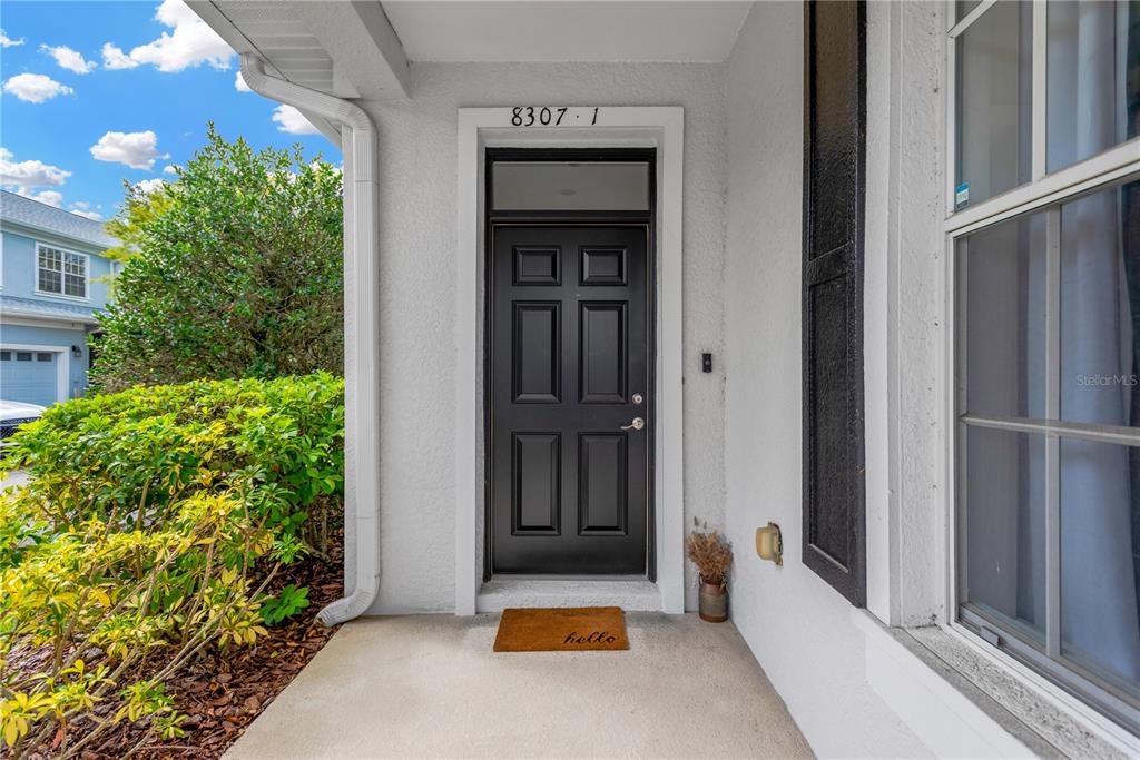 A black front door with a transom window sits on a covered concrete porch — 8307 MANOR CLUB CIRCLE UNIT 1, TAMPA, FL