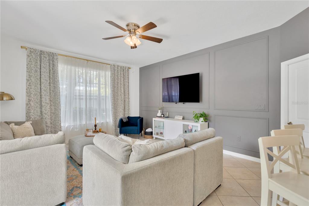 A living room features a gray paneled accent wall, a television, and a sectional sofa — 8307 MANOR CLUB CIRCLE UNIT 1, TAMPA, FL