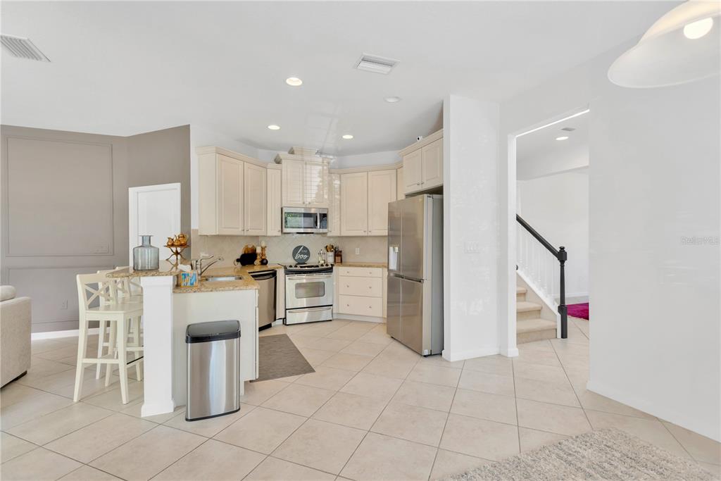 A kitchen with light-colored cabinets, stainless steel appliances, and a breakfast bar with stools — 8307 MANOR CLUB CIRCLE UNIT 1, TAMPA, FL