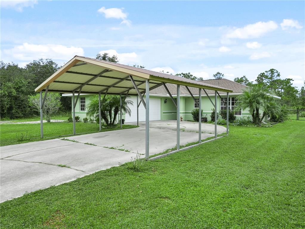 A light green house with a large metal carport stands on a grassy lawn — 3500 HIBISCUS DRIVE, INDIAN LAKE ESTATES, FL