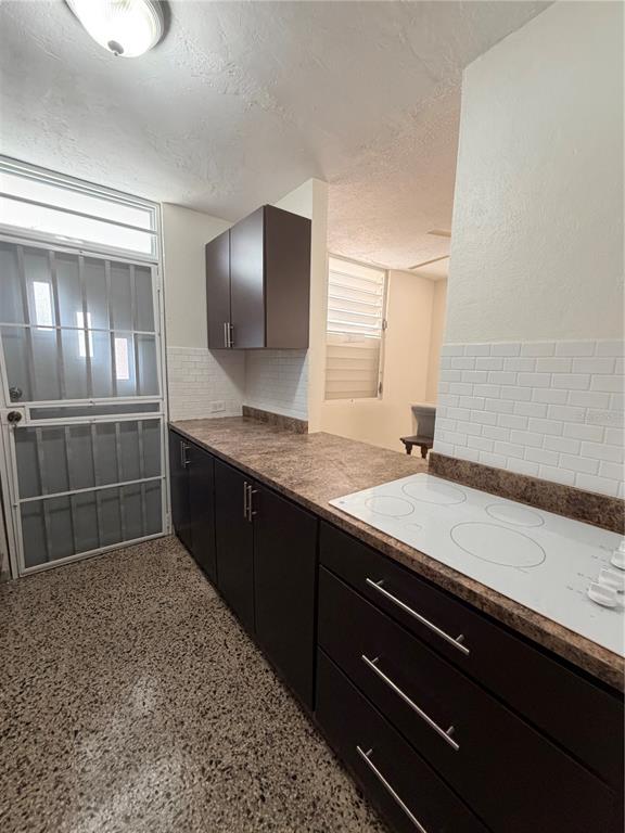 A kitchen features dark brown cabinets, a speckled countertop, a white stovetop, and white backsplash — 163 CALLE VALENCIA, SAN GERMAN, PR