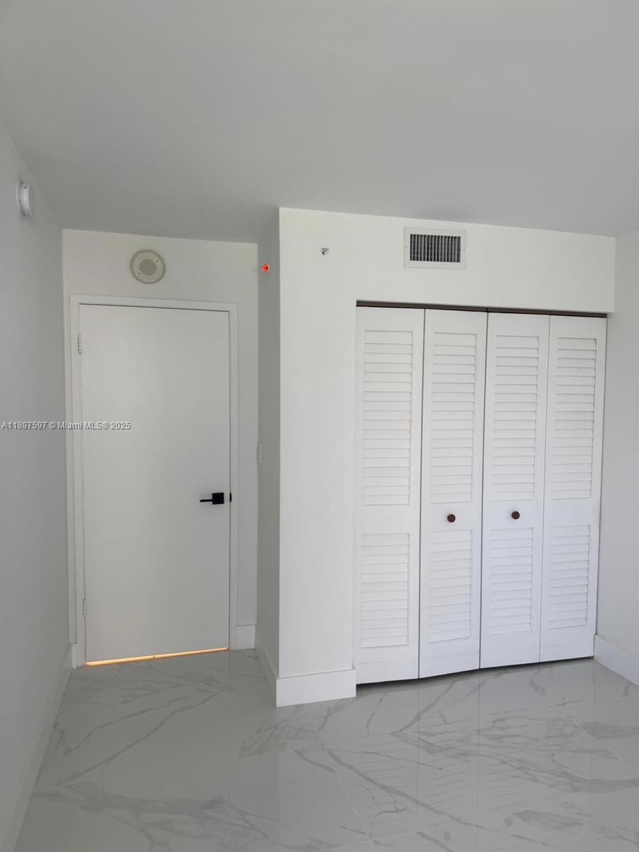 A room features white walls, light-colored marble-patterned tile flooring, a white door, and a louvered closet — 800 N Miami Ave # 901, Miami FL 33136, MIAMI, FL