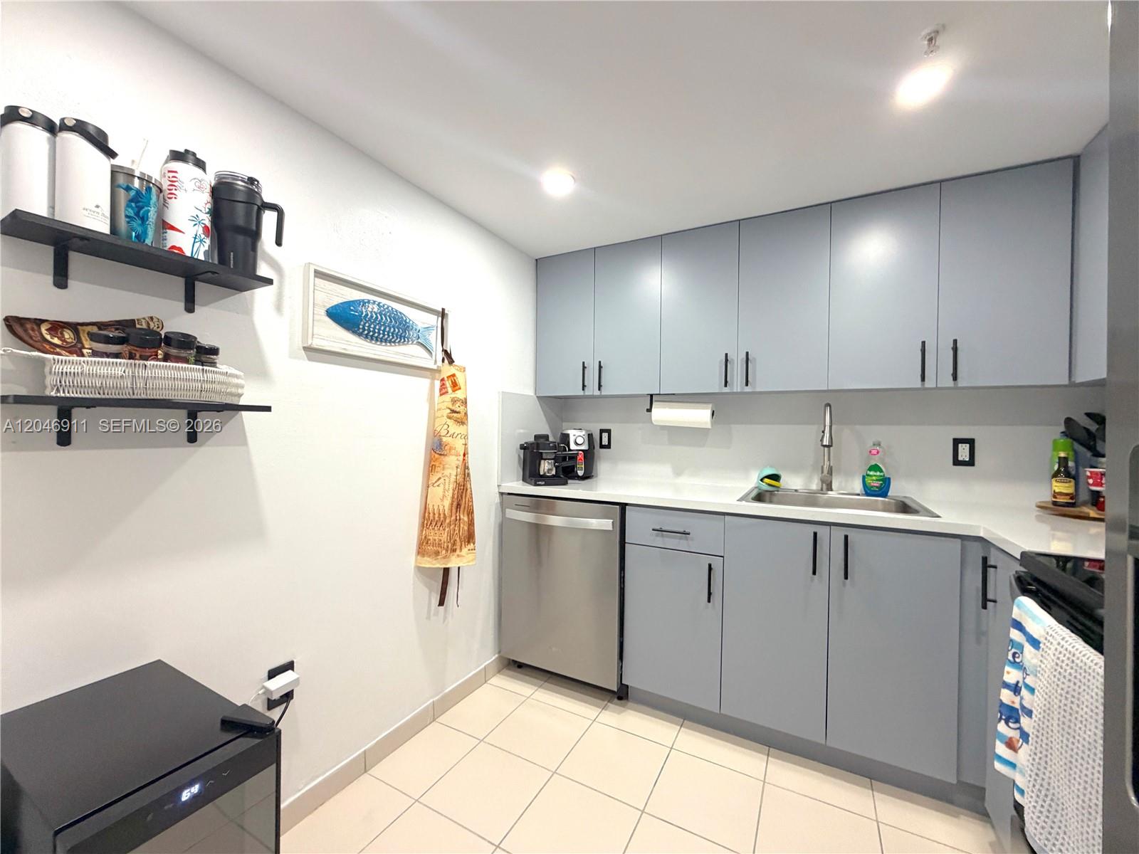 A kitchen features light blue cabinets, stainless steel appliances, and open shelving on the wall — 2829 Indian Creek Dr # 605, Miami Beach FL 33140, MIAMI BEACH, FL
