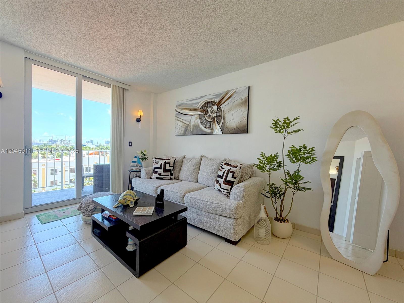 A living room features a light-colored sofa, a dark coffee table, and a large floor mirror — 2829 Indian Creek Dr # 605, Miami Beach FL 33140, MIAMI BEACH, FL