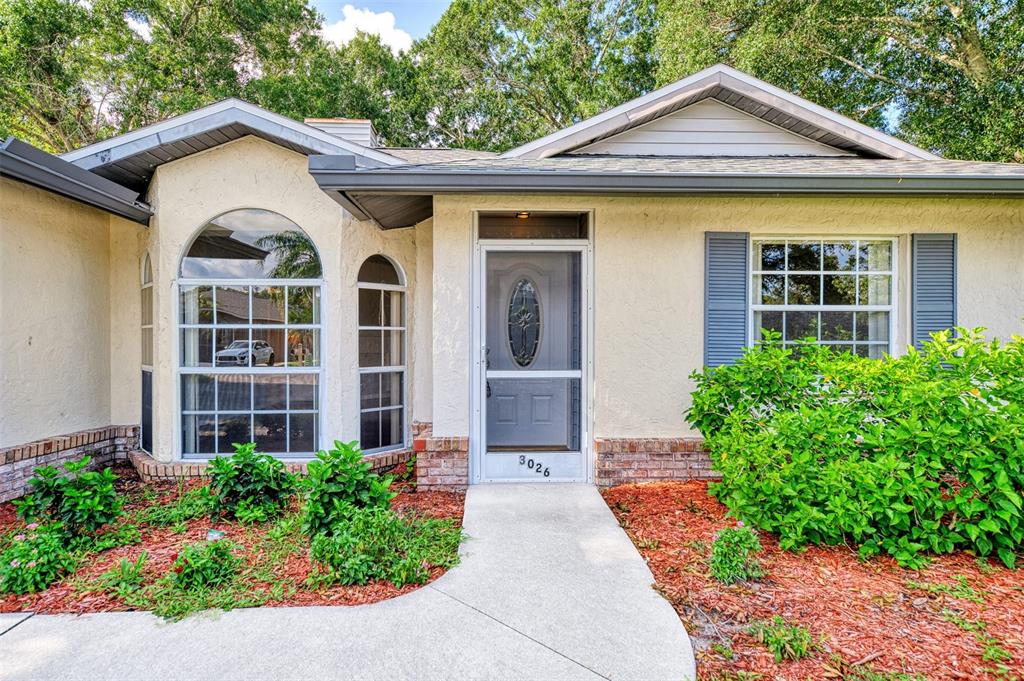 The exterior of a single-story house features a light-colored stucco facade, brick accents, and landscaping — 3026 GRAFTON STREET, SARASOTA, FL