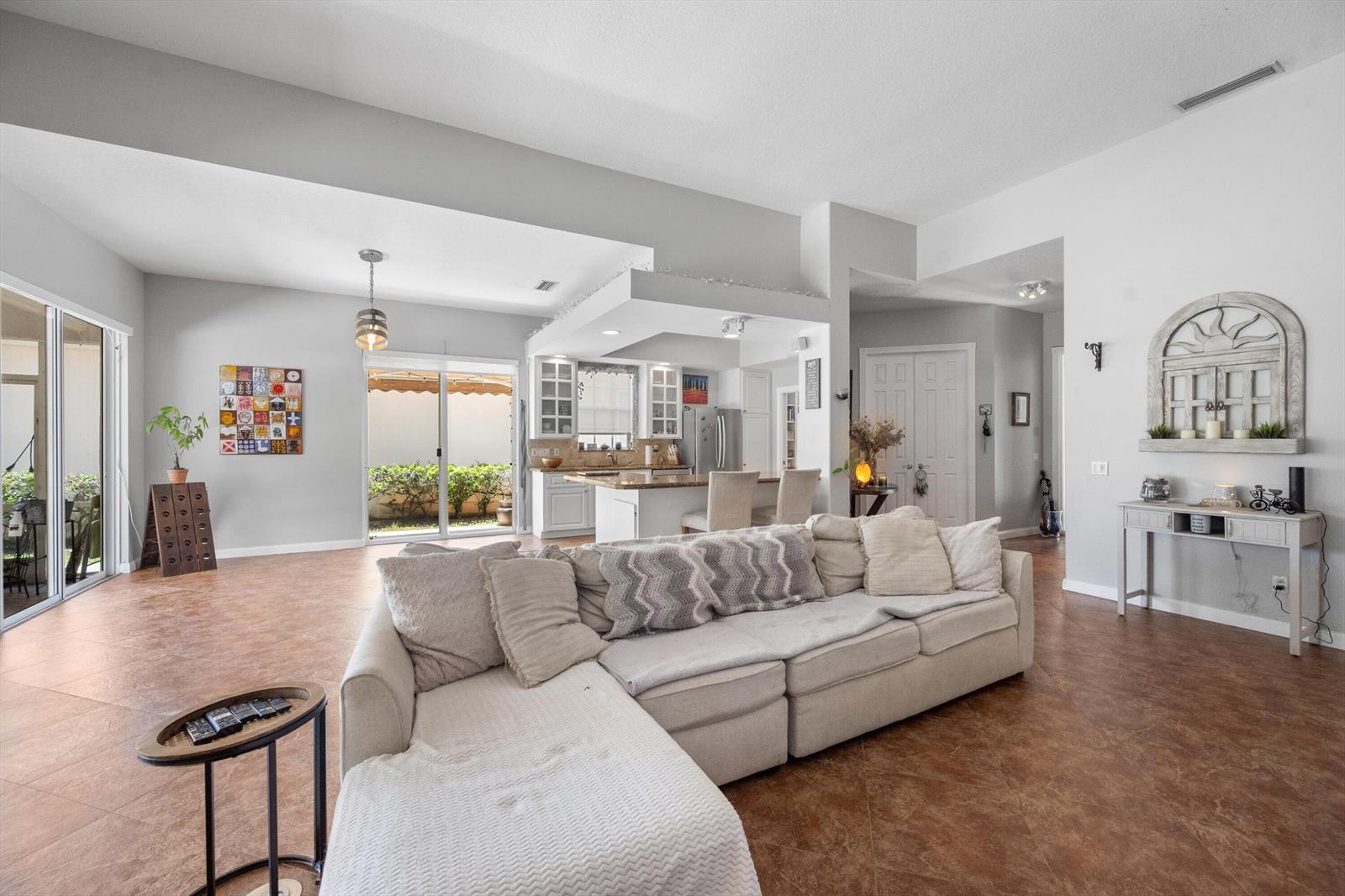 A spacious living room with tile floors features a large sectional sofa and an open kitchen — 2862 Irma Lake Drive, West Palm Beach FL 33411, WEST PALM BEACH, FL