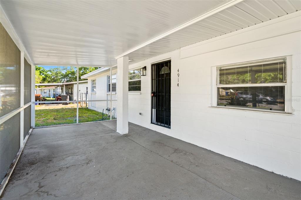 A covered concrete patio features a screened-in side, a white block wall, and a front door — 4914 S 82ND STREET, TAMPA, FL