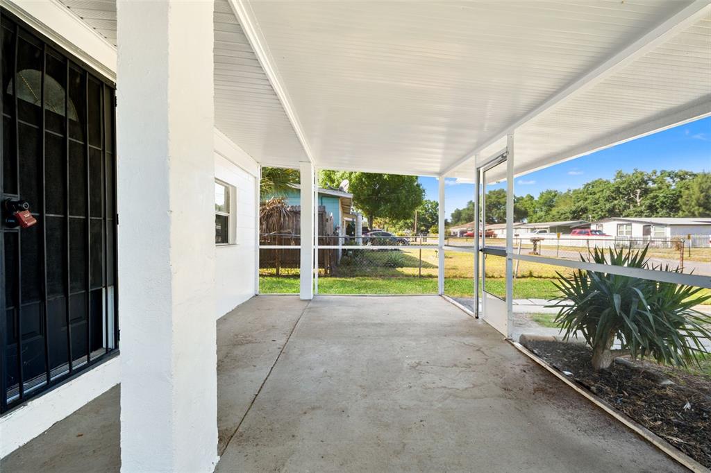 A covered concrete porch features white support columns and a screened-in enclosure — 4914 S 82ND STREET, TAMPA, FL