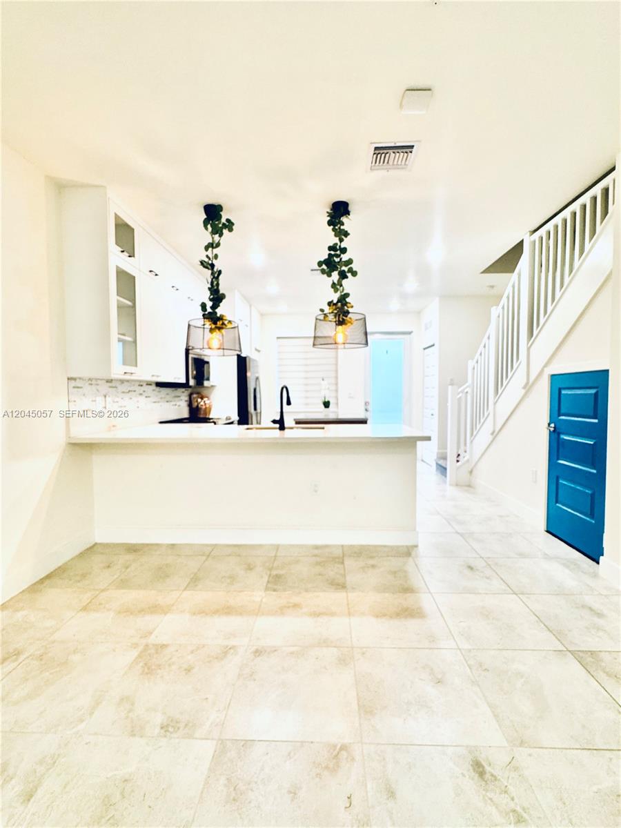 A modern kitchen features white cabinetry, a breakfast bar, and two hanging pendant lights — 10295 NW 64th Ter # 104, Doral FL 33178, DORAL, FL