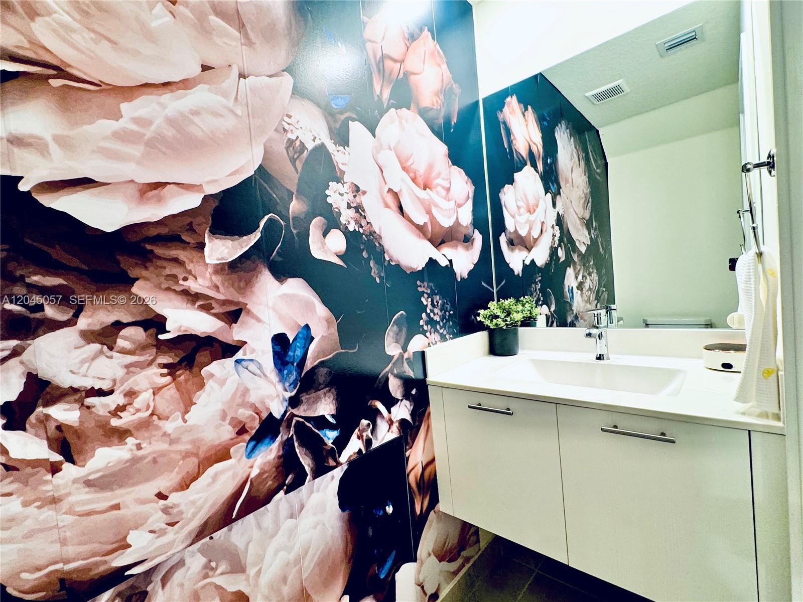 A bathroom features a floral accent wall, a white floating vanity, and a large mirror — 10295 NW 64th Ter # 104, Doral FL 33178, DORAL, FL