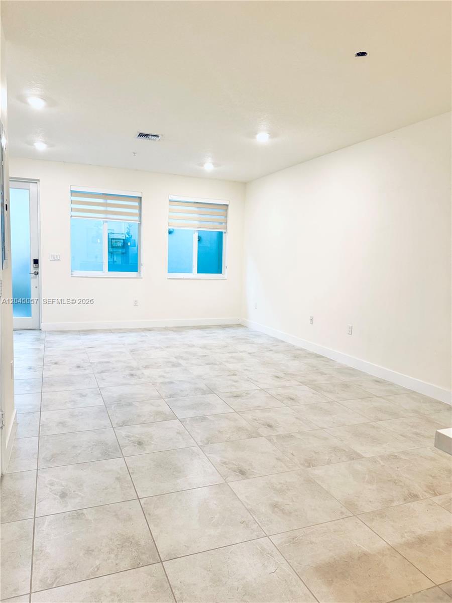 An empty room features light-colored tile flooring, white walls, and two windows with blinds — 10295 NW 64th Ter # 104, Doral FL 33178, DORAL, FL