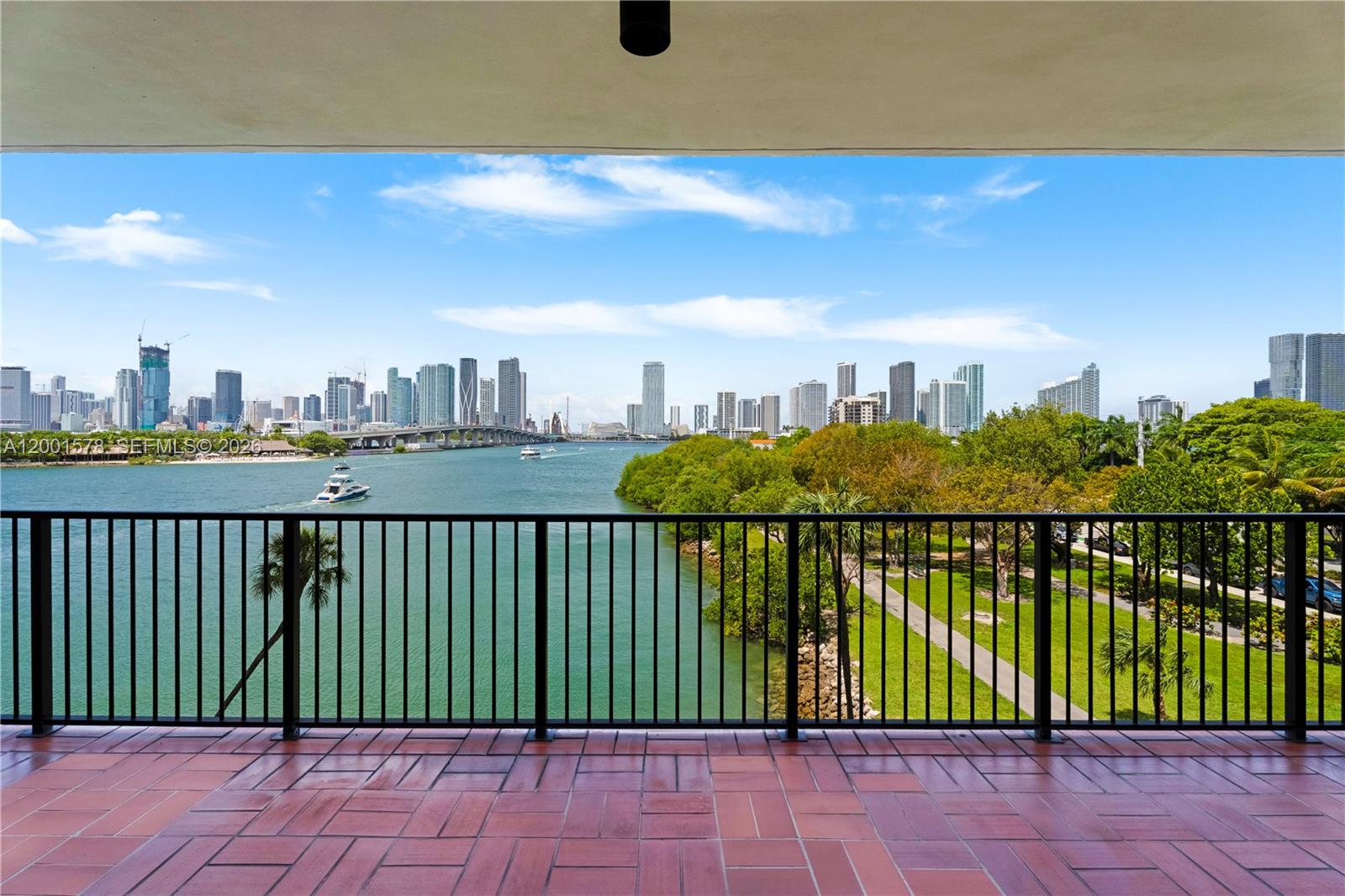 A balcony with red tile flooring overlooks a waterway, park, and city skyline — 1000 Venetian Way # 408, Miami FL 33139, MIAMI, FL