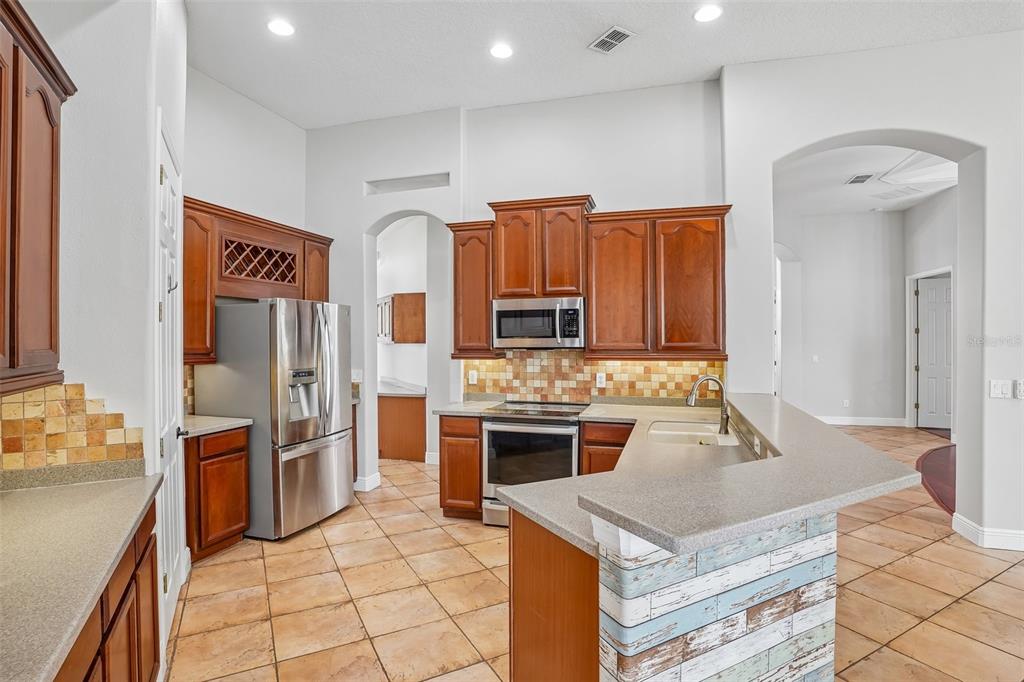 A kitchen features wood cabinets, stainless steel appliances, tile flooring, and a breakfast bar — 910 PARASOL PLACE, OVIEDO, FL