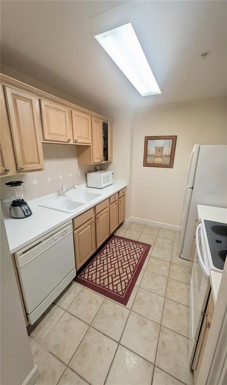A galley kitchen features light wood cabinets, white countertops, a white dishwasher, and tile flooring — 750 N TAMIAMI TRAIL UNIT 1204, SARASOTA, FL