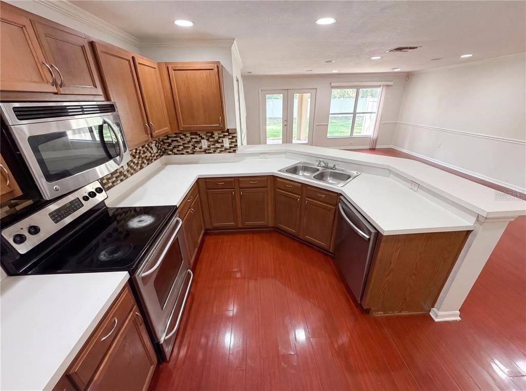 A kitchen with wood cabinets, white countertops, stainless steel appliances, and reddish-brown wood flooring — 2972 ROYAL TUSCAN LANE, VALRICO, FL