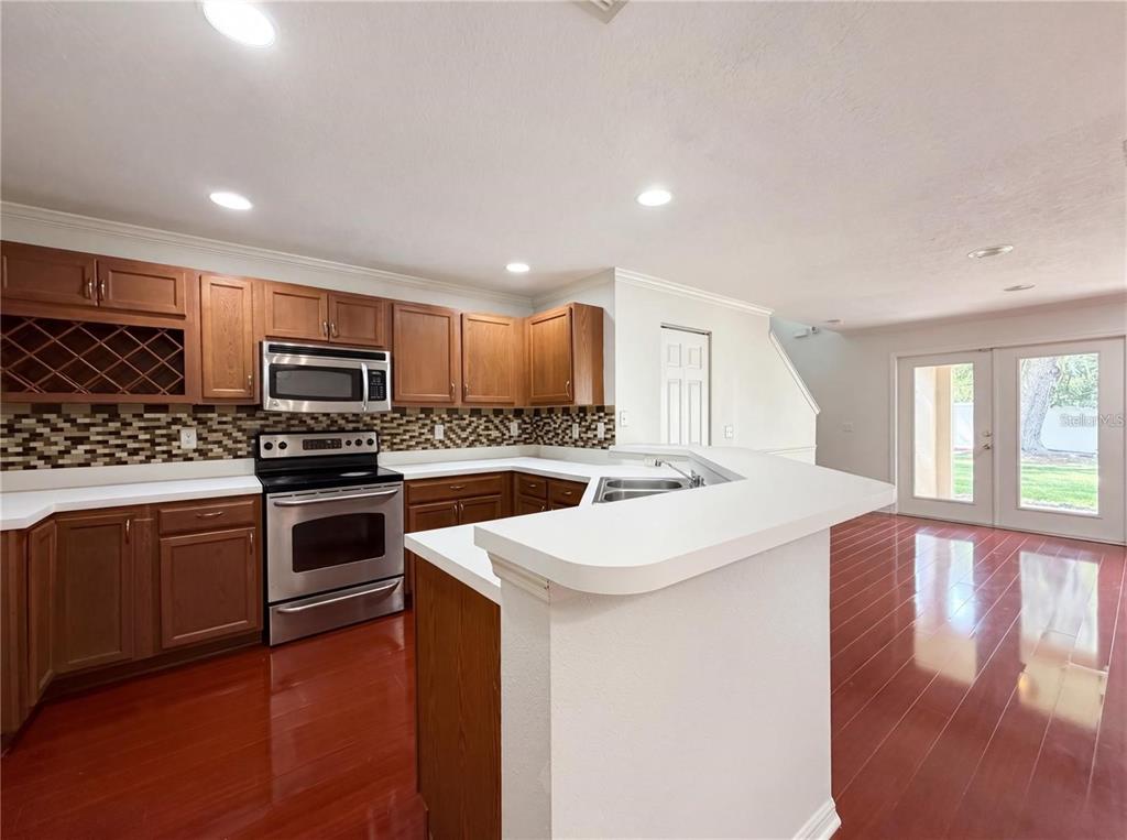A kitchen features wood cabinets, stainless steel appliances, a tile backsplash, and dark wood flooring — 2972 ROYAL TUSCAN LANE, VALRICO, FL