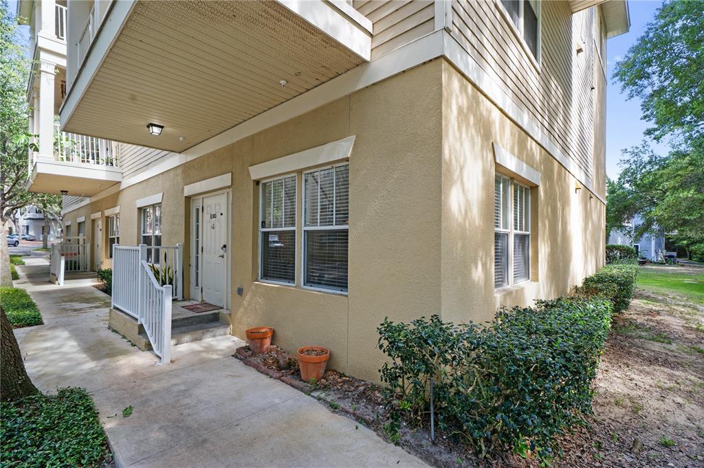A beige stucco apartment building exterior features a covered entryway, white railings, and two potted plants — 9177 SW 52ND ROAD UNIT E-103, GAINESVILLE, FL