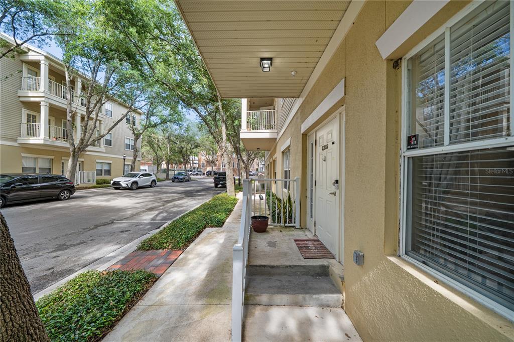 An exterior view of a ground-level apartment entrance with a concrete walkway and stairs — 9177 SW 52ND ROAD UNIT E-103, GAINESVILLE, FL