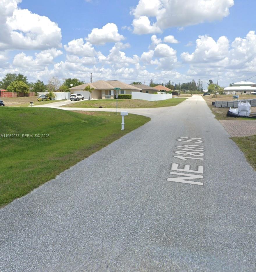A paved street with a painted label leads toward a suburban house with a white fence — 124 NE 18TH ST, Cape Coral FL 33909, CAPE CORAL, FL