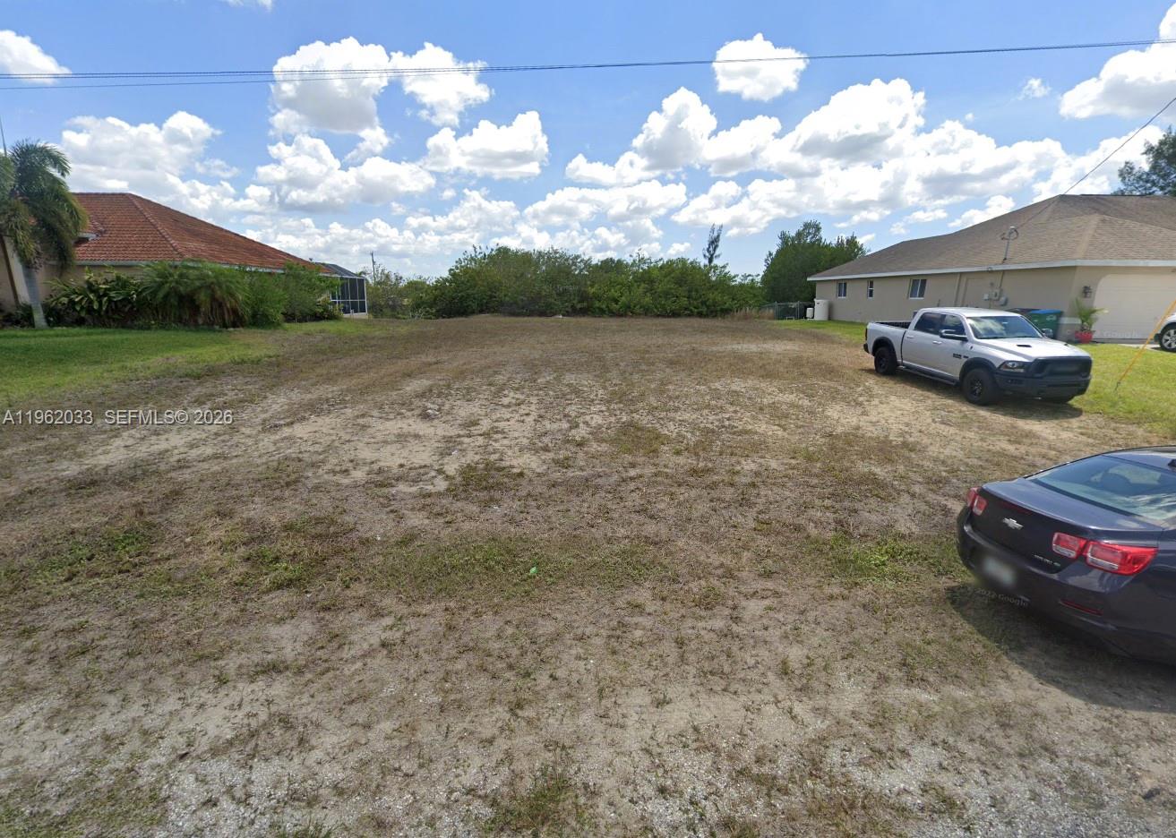 A vacant, sandy residential lot is situated between two houses under a blue sky — 124 NE 18TH ST, Cape Coral FL 33909, CAPE CORAL, FL
