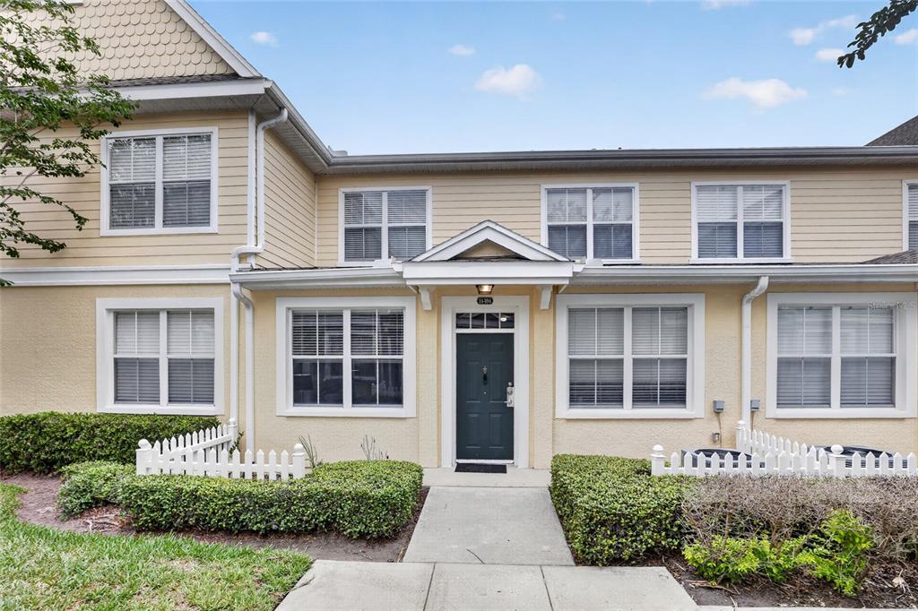 A two-story townhouse exterior with yellow siding, a dark front door, and a white fence — 4006 SAN GALLO DRIVE UNIT 104, KISSIMMEE, FL