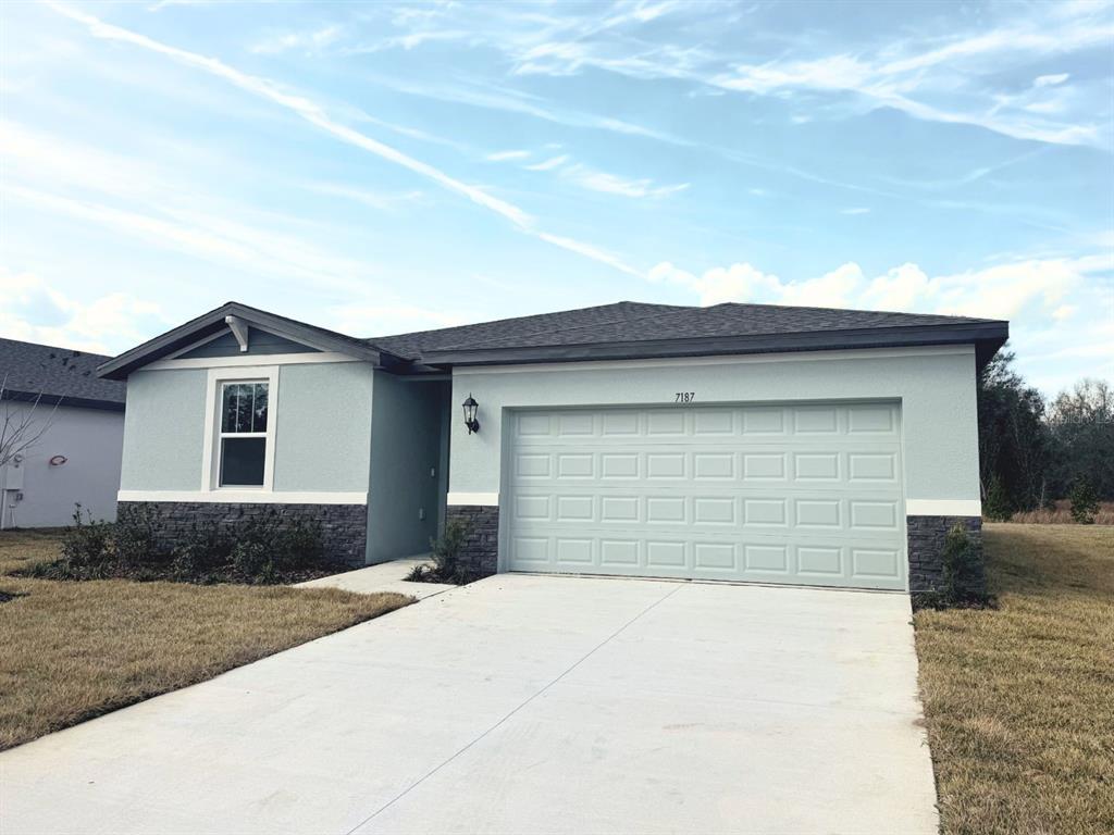 A single-story house with light blue stucco, stone veneer accents, and a two-car garage — 7187 RAY CREEK DRIVE, BROOKSVILLE, FL