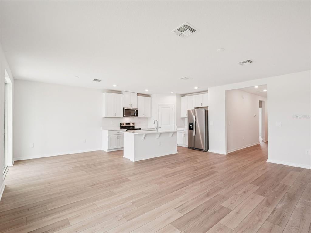 A bright, open-concept kitchen features white cabinetry, stainless steel appliances, and light wood-look flooring — 7187 RAY CREEK DRIVE, BROOKSVILLE, FL