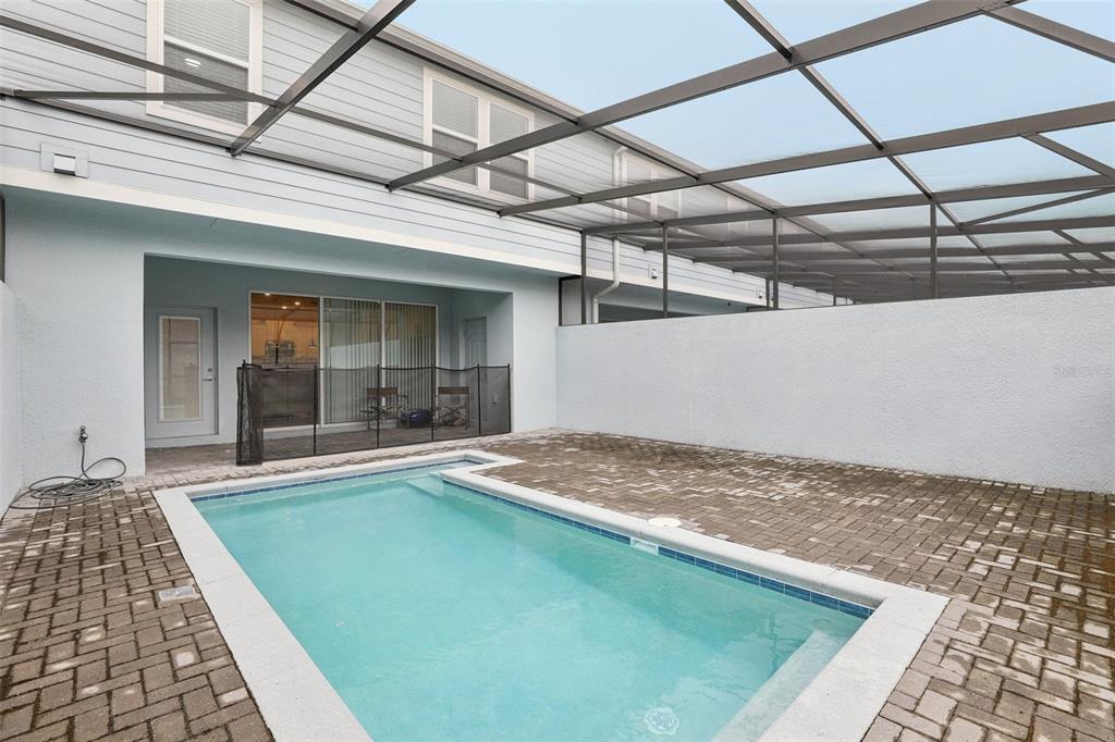 A screened-in patio features a rectangular swimming pool surrounded by brick pavers and a wall — 297 JETTY WAY, DAVENPORT, FL
