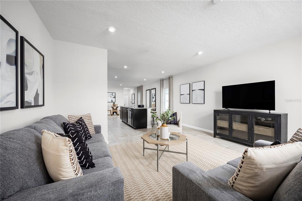 A living room with grey sofas, a coffee table, and a television faces a kitchen — 6944 SUNDIAL DRIVE, LAKELAND, FL