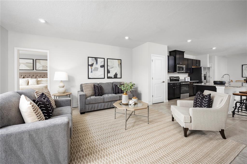 A living room with gray sofas, a beige armchair, and an open kitchen with dark cabinets — 6944 SUNDIAL DRIVE, LAKELAND, FL