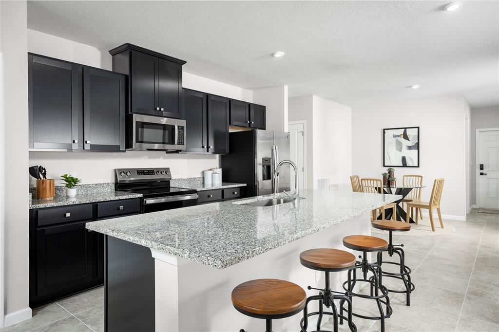 A kitchen features black cabinets, granite countertops, a large island with stools, and stainless appliances — 6944 SUNDIAL DRIVE, LAKELAND, FL