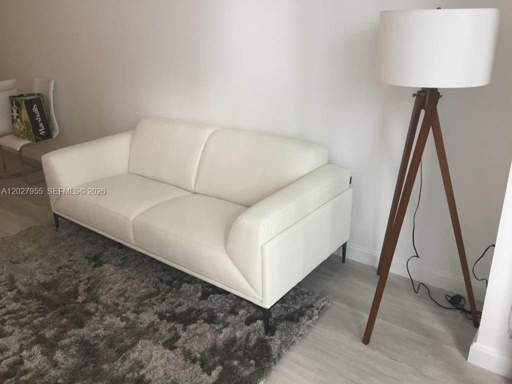A white sofa sits on a gray rug next to a wooden tripod floor lamp — 55 SW 9th St # 2709, Miami FL 33130, MIAMI, FL