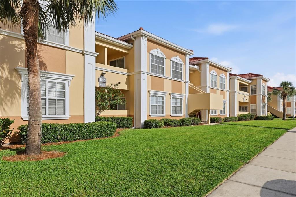 A multi-story apartment building with tan stucco walls and white trim sits behind a lawn — 1015 VILLAGIO CIRCLE UNIT 202, SARASOTA, FL