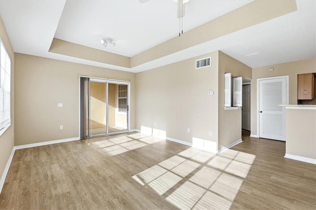 An empty living room features light wood-look flooring, a tray ceiling, and sliding glass doors — 1015 VILLAGIO CIRCLE UNIT 202, SARASOTA, FL