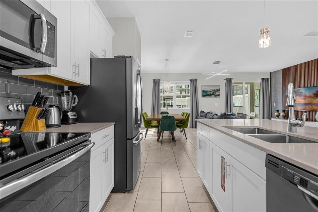 A modern kitchen with white cabinets and stainless steel appliances opens to a dining area — 4823 DEDICATION STREET, KISSIMMEE, FL