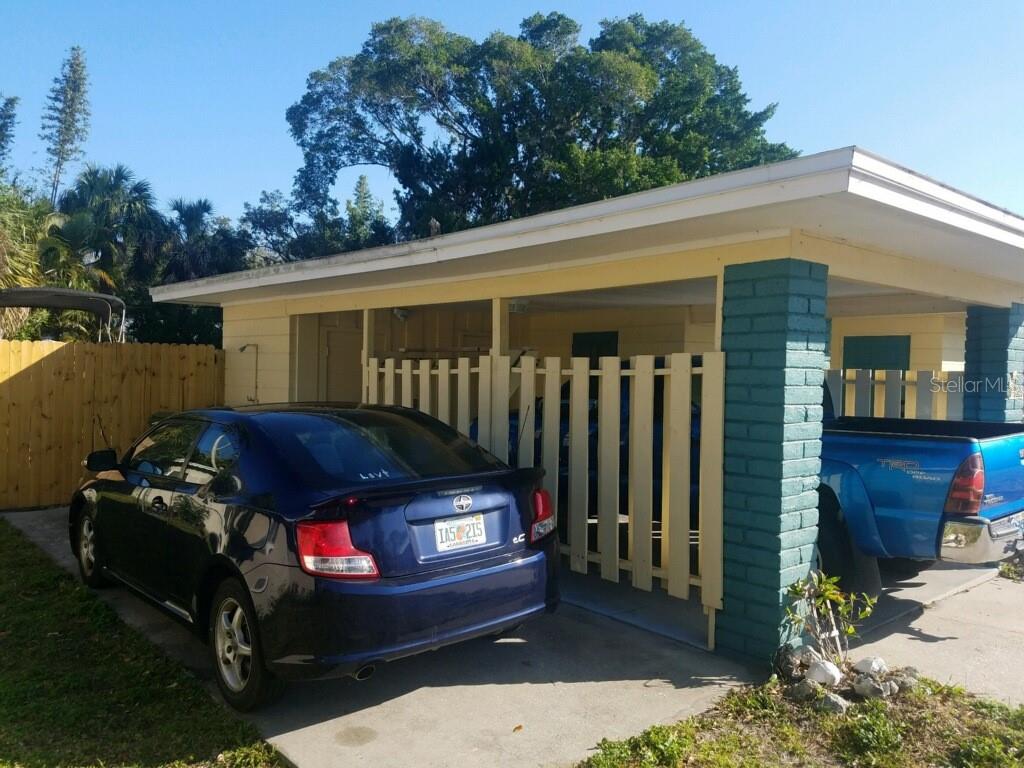 A blue car is parked in a driveway next to a carport with a wooden fence — 2165 SUNNYSIDE LANE, SARASOTA, FL