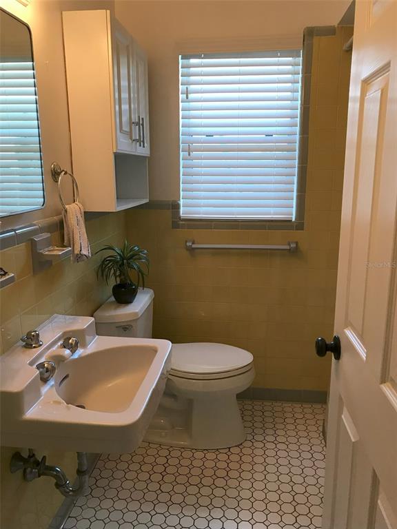 A bathroom features a pedestal sink, a toilet, and yellow wall tiles with white flooring — 2165 SUNNYSIDE LANE, SARASOTA, FL