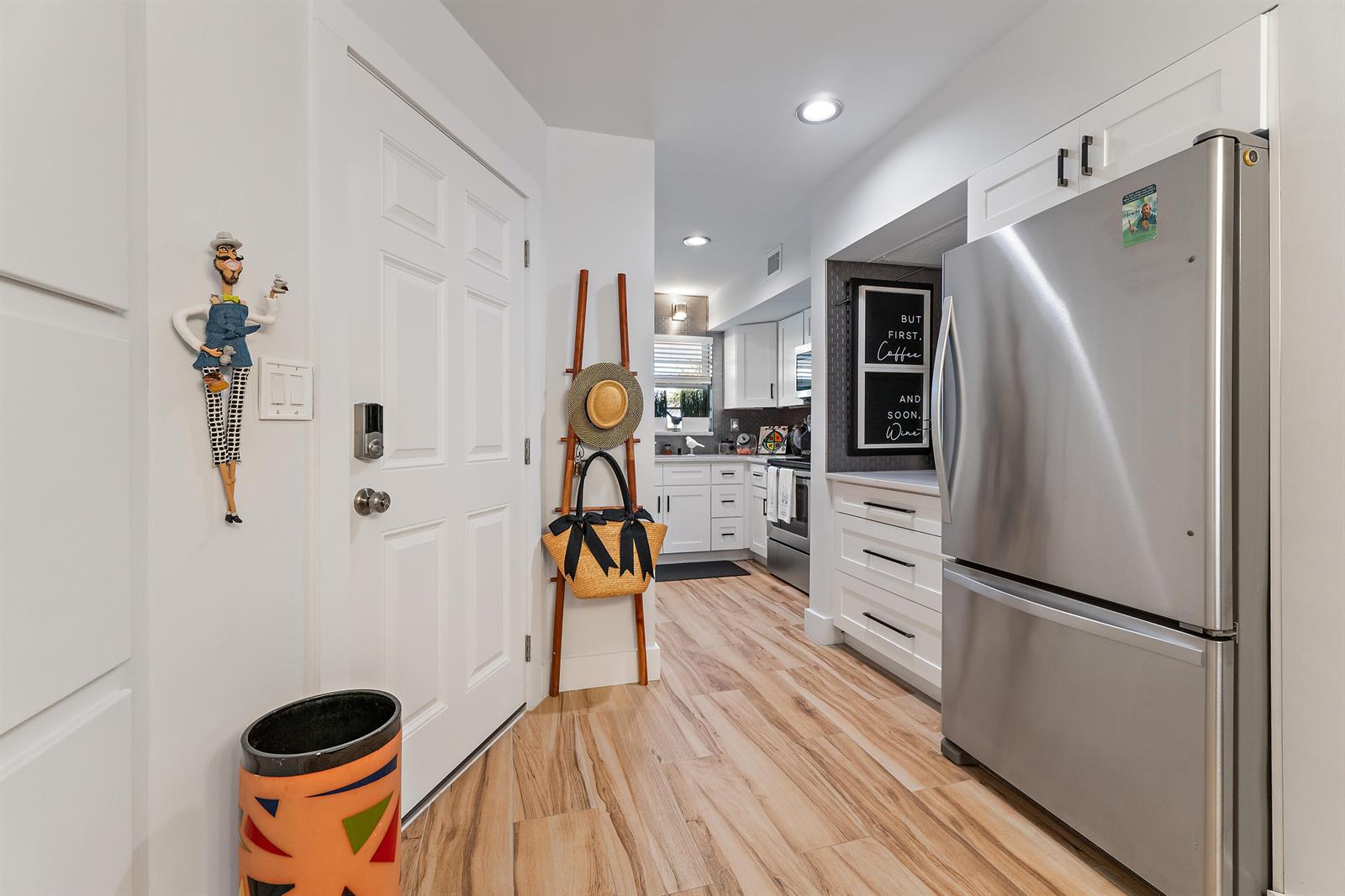 A kitchen with white cabinets, stainless steel appliances, and wood-look flooring viewed from a hallway — 50 Celestial Way # 310, Juno Beach FL 33408, JUNO BEACH, FL