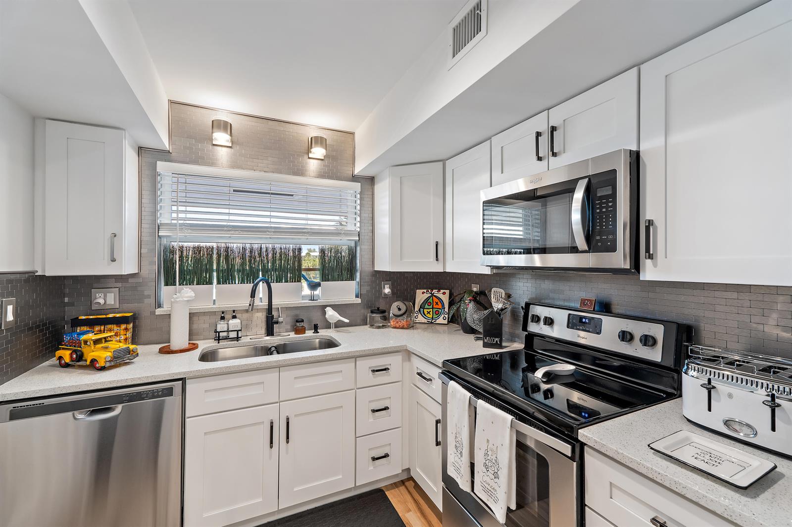 A kitchen features white cabinetry, stainless steel appliances, a gray tile backsplash, and quartz countertops — 50 Celestial Way # 310, Juno Beach FL 33408, JUNO BEACH, FL