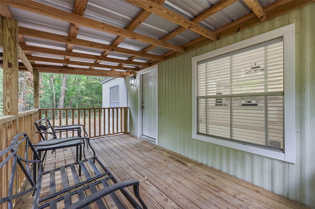A wooden porch with metal roofing, a white door, and outdoor furniture overlooks a wooded area — 264 SW CENTRAL TERRACE, FORT WHITE, FL